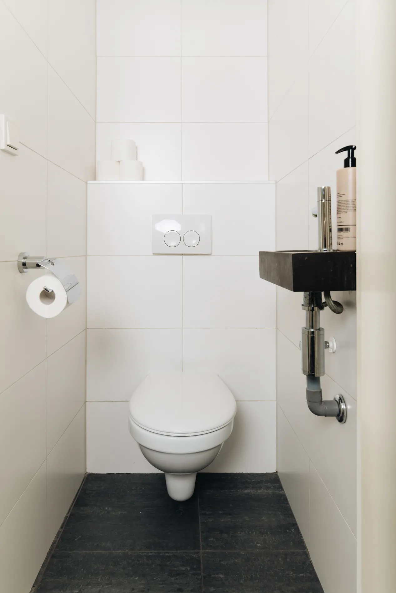 Modern, separaat toilet met witte tegels en een compact fonteintje.